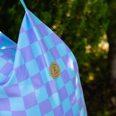 Mochila azul claro e lilás com padrão quadriculado e etiqueta redonda