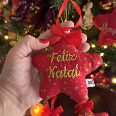 Enfeite de Natal em forma de estrela vermelha com texto Feliz Natal em dourado.