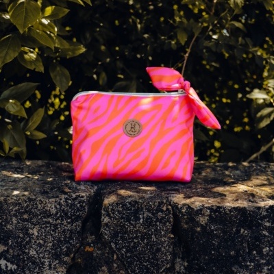 Necessaire rosa com riscas laranja sobre pedra com plantas ao fundo