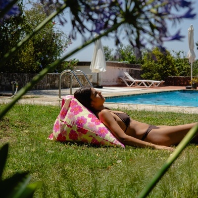 Almofada floral rosa e amarela num jardim junto a piscina com mulher a repousar