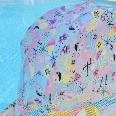 Bolsa de praia colorida com padrão de flamingos e bolso de rede junto a uma piscina