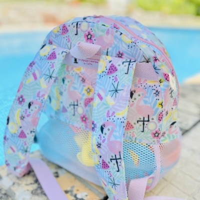 Mochila infantil colorida com padrão de flamingos e melancias junto a piscina