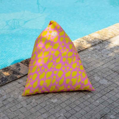 Pufe triangular cor-de-rosa com manchas amarelas junto a piscina azul