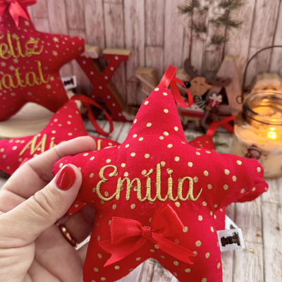 Estrela de tecido vermelha com bordado Emília e decorada ao fundo com elementos natalícios