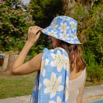 Chapéu e toalha de praia azuis com flores brancas e amarelas usados por pessoa junto a piscina
