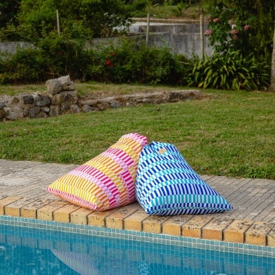 Dois pufes coloridos junto à piscina numa área exterior com relva e plantas