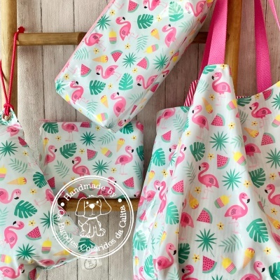 Conjunto de bolsas coloridas com padrão de flamingos e folhas penduradas numa parede de madeira.
