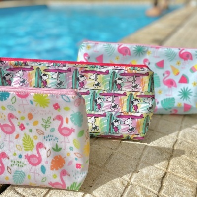 Três sacos cosméticos coloridos com padrões de flamingos, desenhos animados e frutas tropicais junto a uma piscina