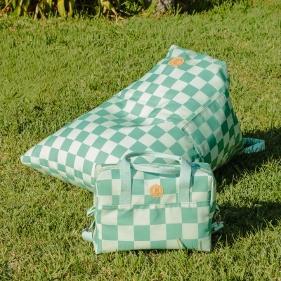 Pufe e bolsa quadriculados verdes e brancos na relva com plantas ao fundo