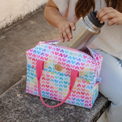 Bolsa térmica colorida com padrão de corações e garrafa térmica metálica prateada a ser colocada dentro