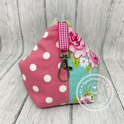 Bolsa artesanal em tecido rosa com bolas brancas e flores rosa sobre fundo azul claro com alça xadrez rosa e branco e fecho metálico
