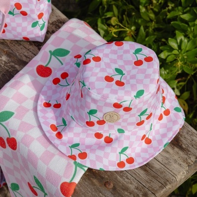 Chapéu de balde rosa com padrão de cerejas em fundo xadrez, sobre toalha com padrão igual