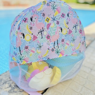 mochila infantil azul claro com flamingos cor-de-rosa e bolso em rede branco ao lado de piscina