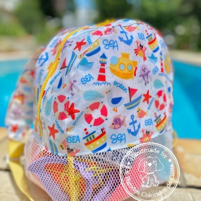 Mochila infantil colorida com padrão marítimo e parte inferior em rede branca ao lado de piscina