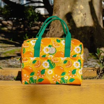 Mala de mão amarela com padrão laranja e verde apoiada num muro amarelo ao ar livre