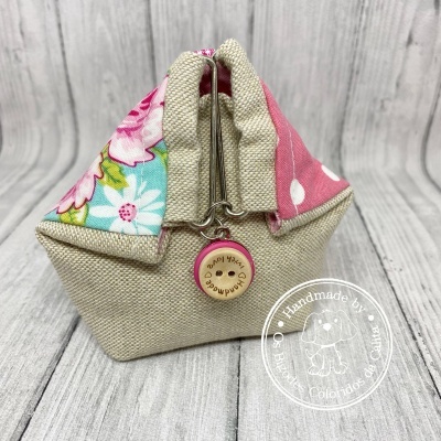 Bolsa pequena em tecido bege com detalhes em rosa e azul floral, fecho metálico e botão em madeira com texto gravado