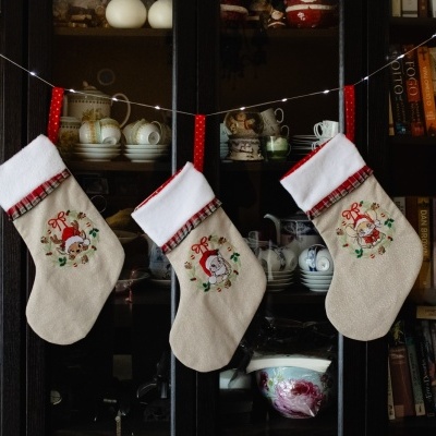 Três meias de Natal bordadas penduradas em móvel com louças e livros ao fundo