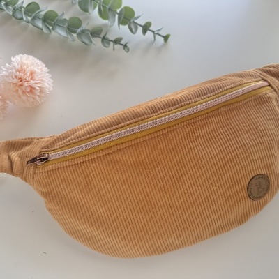 Pochete castanha em veludo cotelê com fecho éclair bege em fundo branco com flores e folhagem.