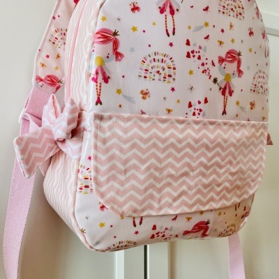 Mochila infantil rosa com estampa de bonecas e bolso frontal com padrão zigzag