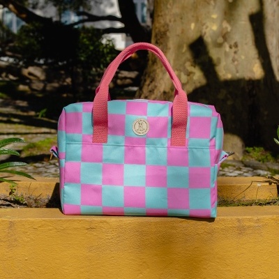 Mala de tecido azul e rosa com padrão xadrez e alças rosa sobre muro amarelo ao ar livre