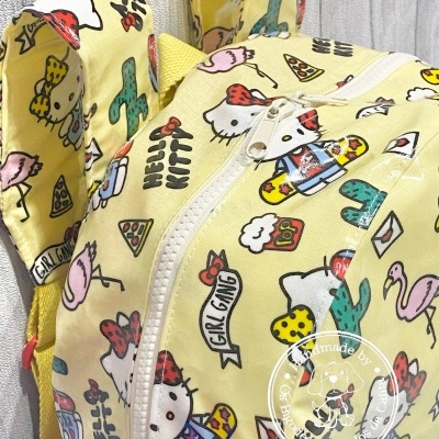 Mochila amarela com padrão de Hello Kitty, frases e imagens coloridas sobre fundo de madeira