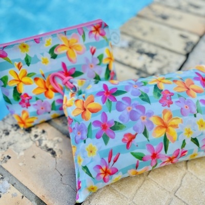 Duas bolsas ou necessaires com padrão floral colorido em fundo azul claro junto a uma piscina.