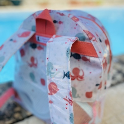 Mochila infantil branca com padrão colorido de peixes, polvos e caranguejos junto a piscina