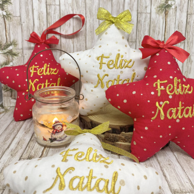 Almofadas star-shaped vermelha e branca com pontos dourados e texto Feliz Natal junto a castiçal com vela acesa
