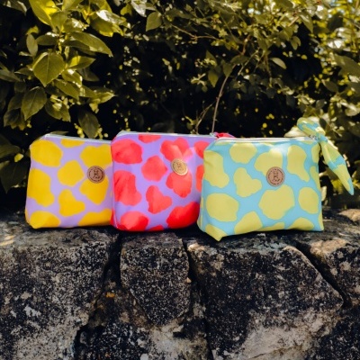 Três bolsas coloridas com padrão de manchas apoiadas em pedra.