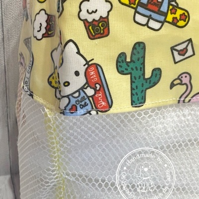 Mochila amarela com desenhos divertidos e parte inferior em rede branca com etiqueta redonda de produto artesanal