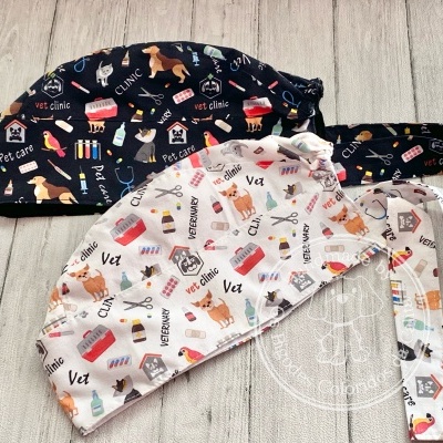 Dois bonés cirúrgicos com estampados veterinários, branco e preto, sobre superfície de madeira clara