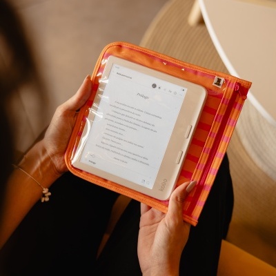 Leitor de e-books branco dentro de bolsa transparente alaranjada listrada segurada pelas mãos.