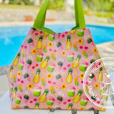 Bolsa de tecido rosa com padrão de frutas e alças verdes, perto de piscina