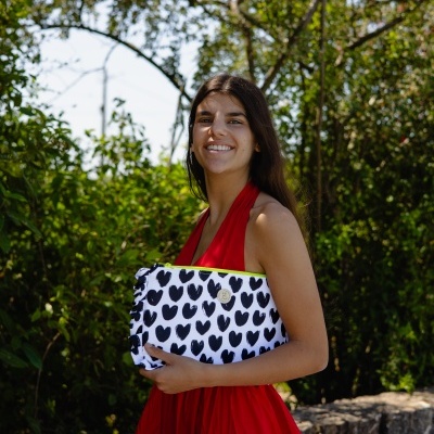 Mulher com vestido vermelho a segurar mala de mão branca com corações pretos em ambiente exterior