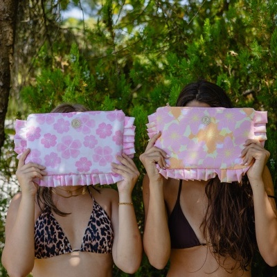 Duas mulheres seguram bolsas com padrão floral rosa e amarelo escondendo o rosto, ao ar livre