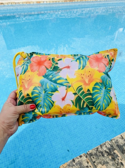 Mala pequena com padrão floral a ser segurada sobre piscina azul