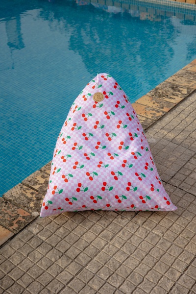 Almofada triangular rosa com padrão de cerejas ao lado de piscina azul