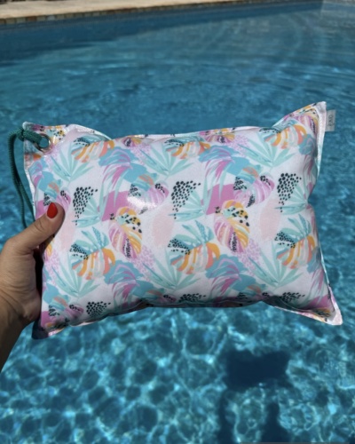 Bolsa almofada com padrão colorido de folhas e texturas segurada sobre piscina azul