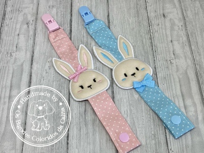 Dois clips de chupeta em tecido cor-de-rosa e azul com rosto de coelho e laços
