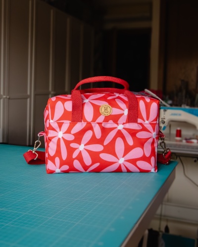 Bolsa vermelha com padrão de flores rosas e alças vermelhas em mesa verde