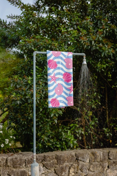 Suporte de chuveiro exterior metálico com toalha decorada e natureza ao fundo