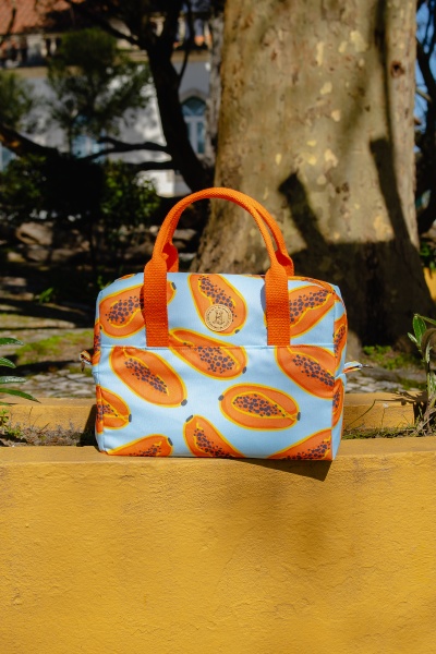 Mala azul com padrão de papaias e alças laranja num ambiente exterior