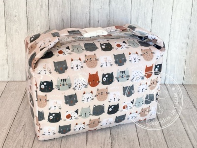 Bolsa retangular com padrão de gatos coloridos em tecido sobre fundo de madeira.