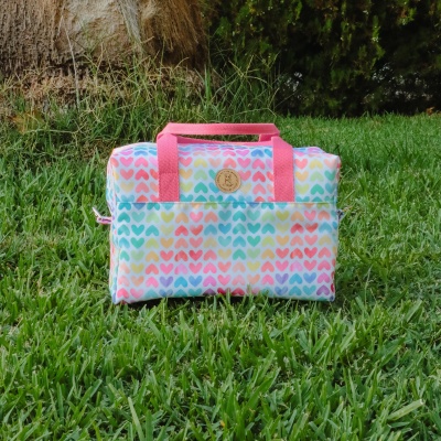 Mala quadrada colorida com padrão de corações e alças cor-de-rosa sobre relva