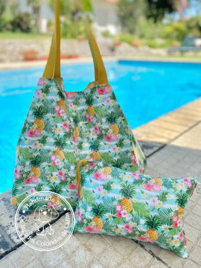Saco e carteira estampados com abacaxis e flores junto a piscina