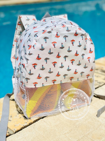 Mochila branca com padrão de barcos e guarda-sóis junto a uma piscina.