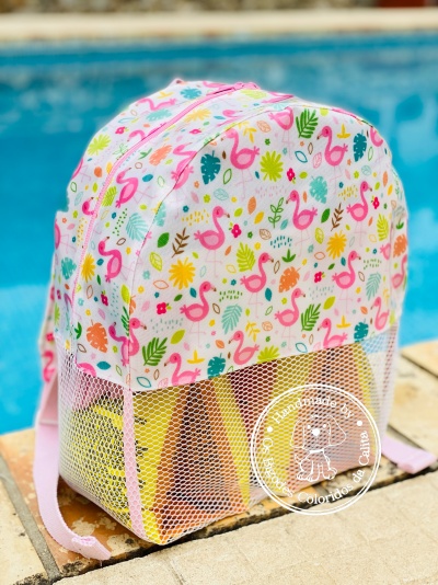 Mochila infantil colorida com padrão de flamingos e folhas perto de piscina