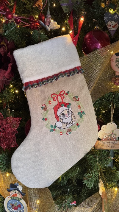 Meia de Natal bege com parte branca felpuda e bordado de coelho, pendurada numa árvore de Natal com decorações vermelhas e douradas.