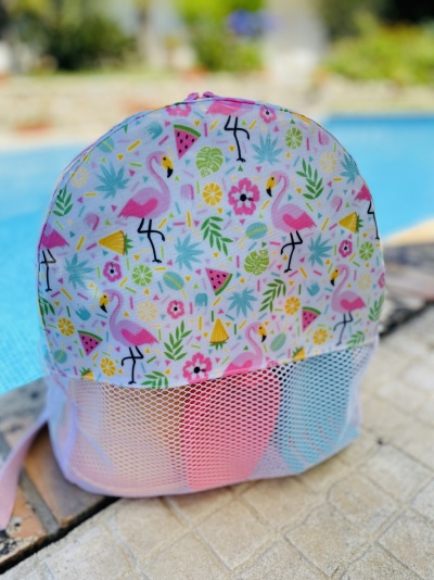 Mochila colorida com padrão de flamingos, melancia e flores, junto a piscina