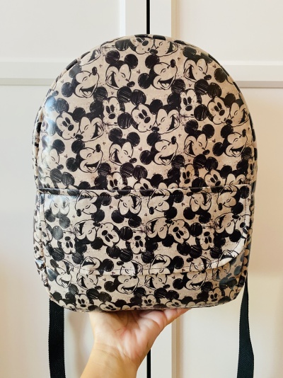 Mochila preta e branca com padrão de Mickey Mouse segura por uma mão
